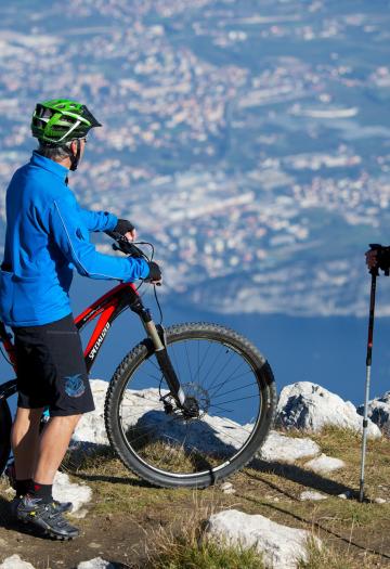 Due persone ammirano il panorama montano, una con bici, l'altra con bastoncini da trekking.