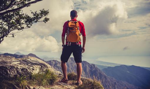 Wanderer mit Rucksack auf dem Berggipfel, bewundert die Aussicht.