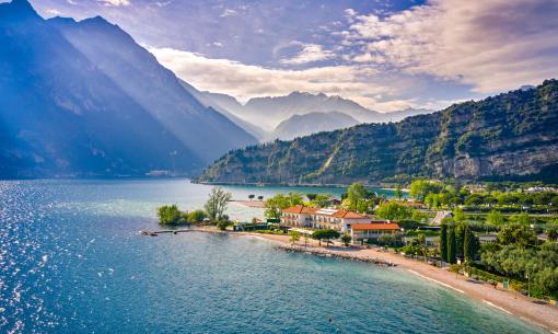 Lake landscape with mountains, beach, and sunny sky.