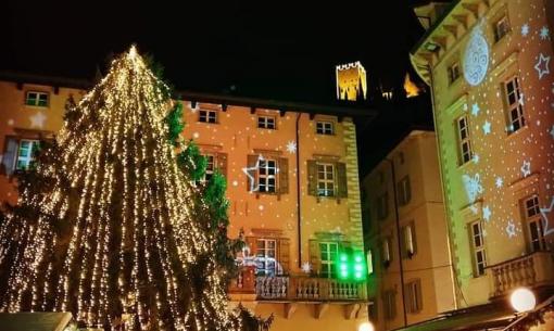 Albero di Natale illuminato in una piazza di notte con decorazioni festive.